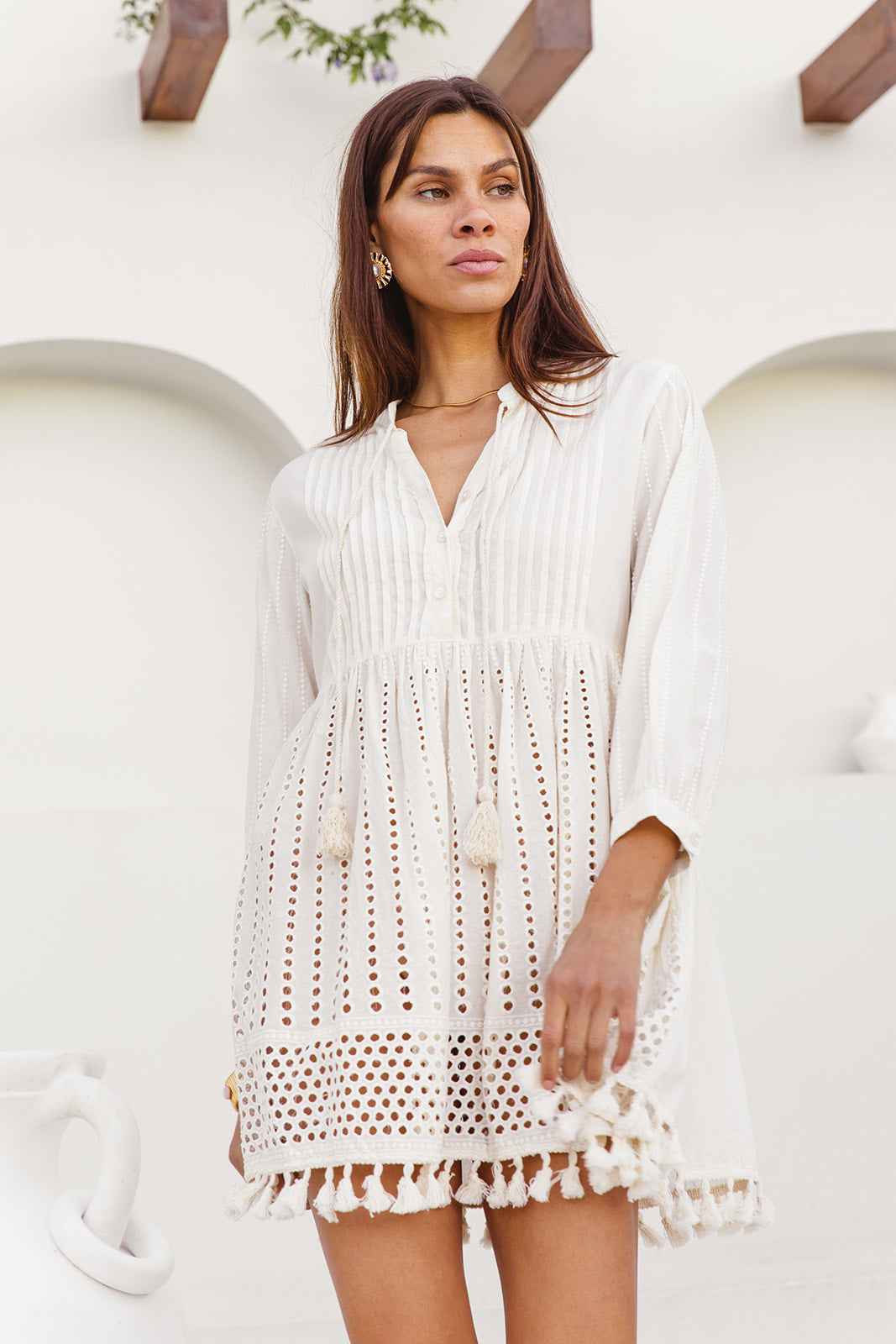 Woman wearing a white cotton cover-up dress against a white wall.