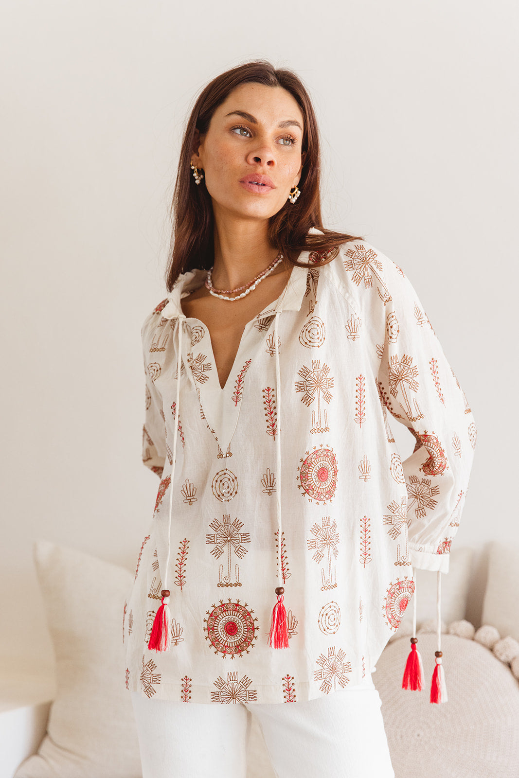 Woman wearing a white embroidered blouse with red details on a neutral background