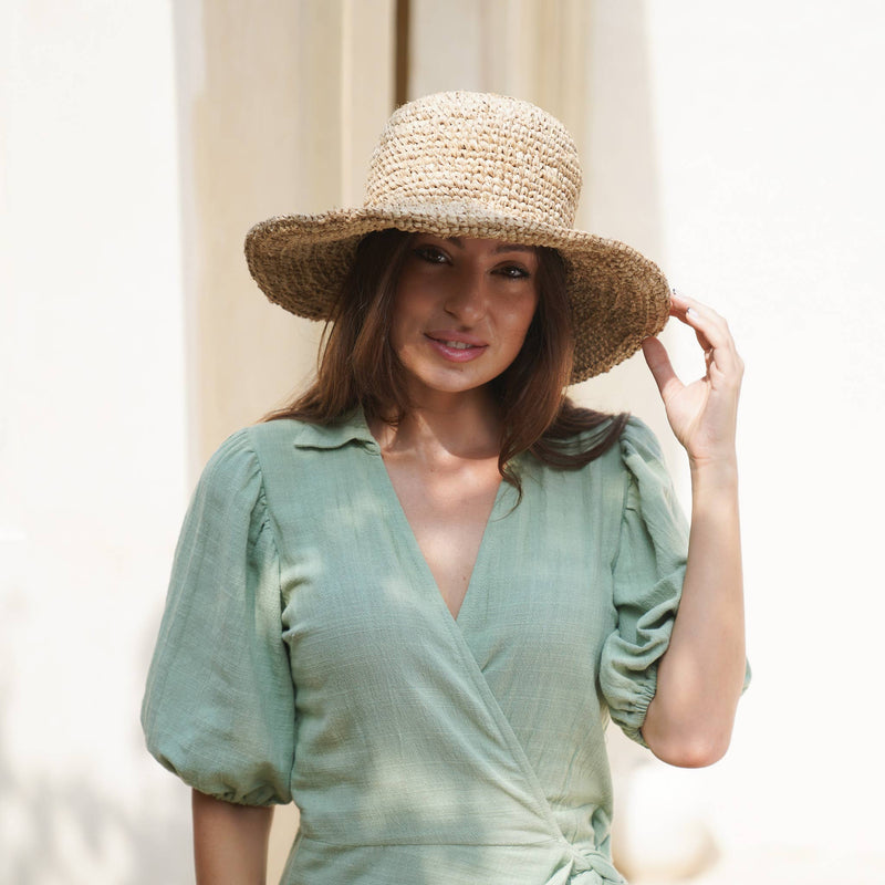 Woman wearing a straw hat and green dress against a neutral background