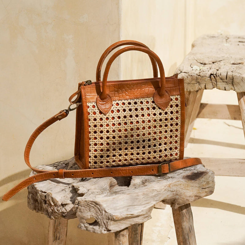 Brown woven handbag with leather straps on a wooden surface