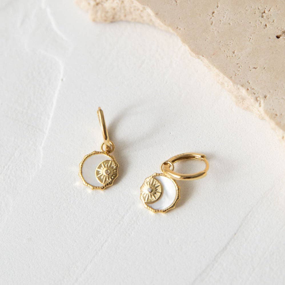 Gold earrings with moon and sun designs on a white surface