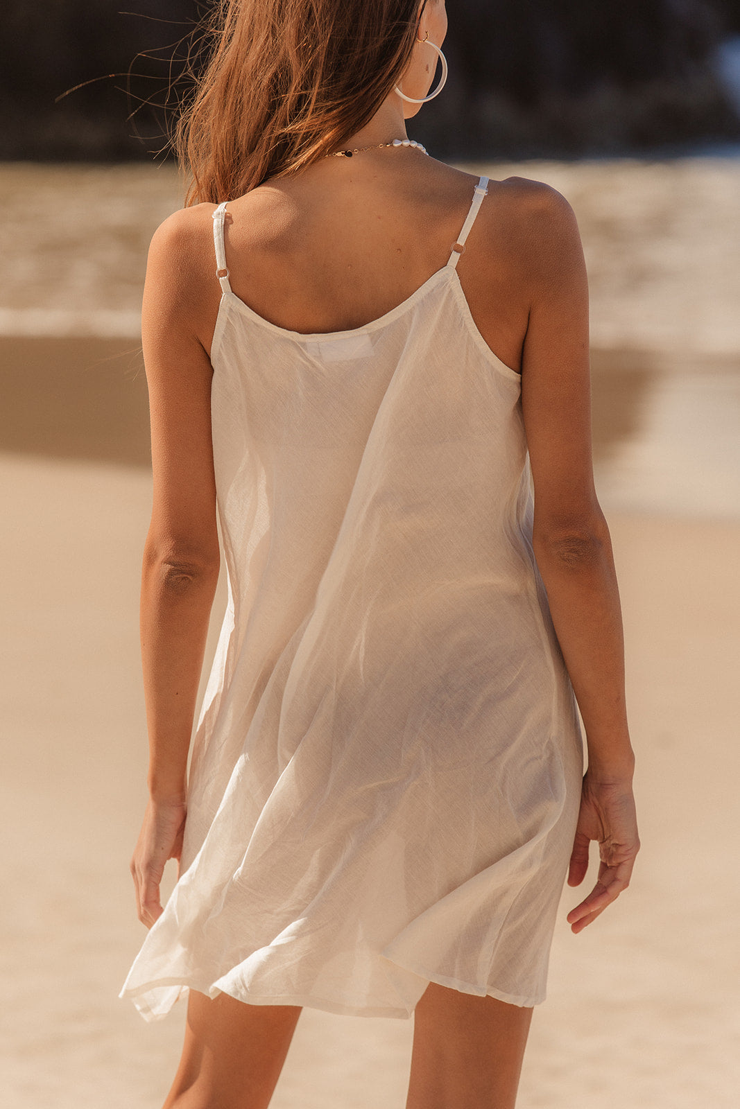 Woman wearing a sheer white slip dress on a beach.