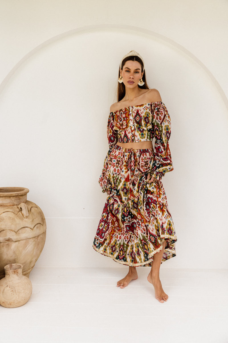 Woman wearing a geometric pattern skirt standing next to a large ceramic jar against a white background