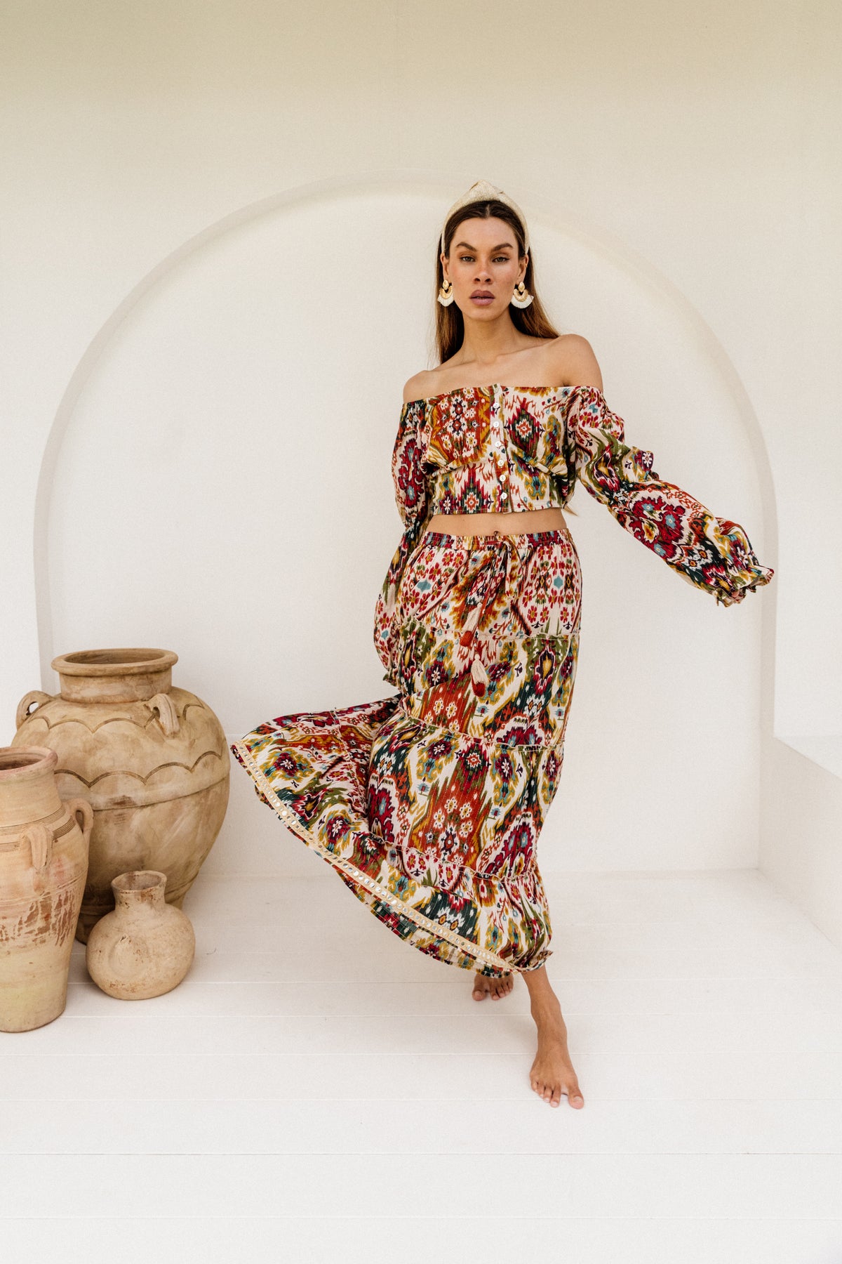Woman in a colourful patterned dress standing in front of a white arch with clay pots.