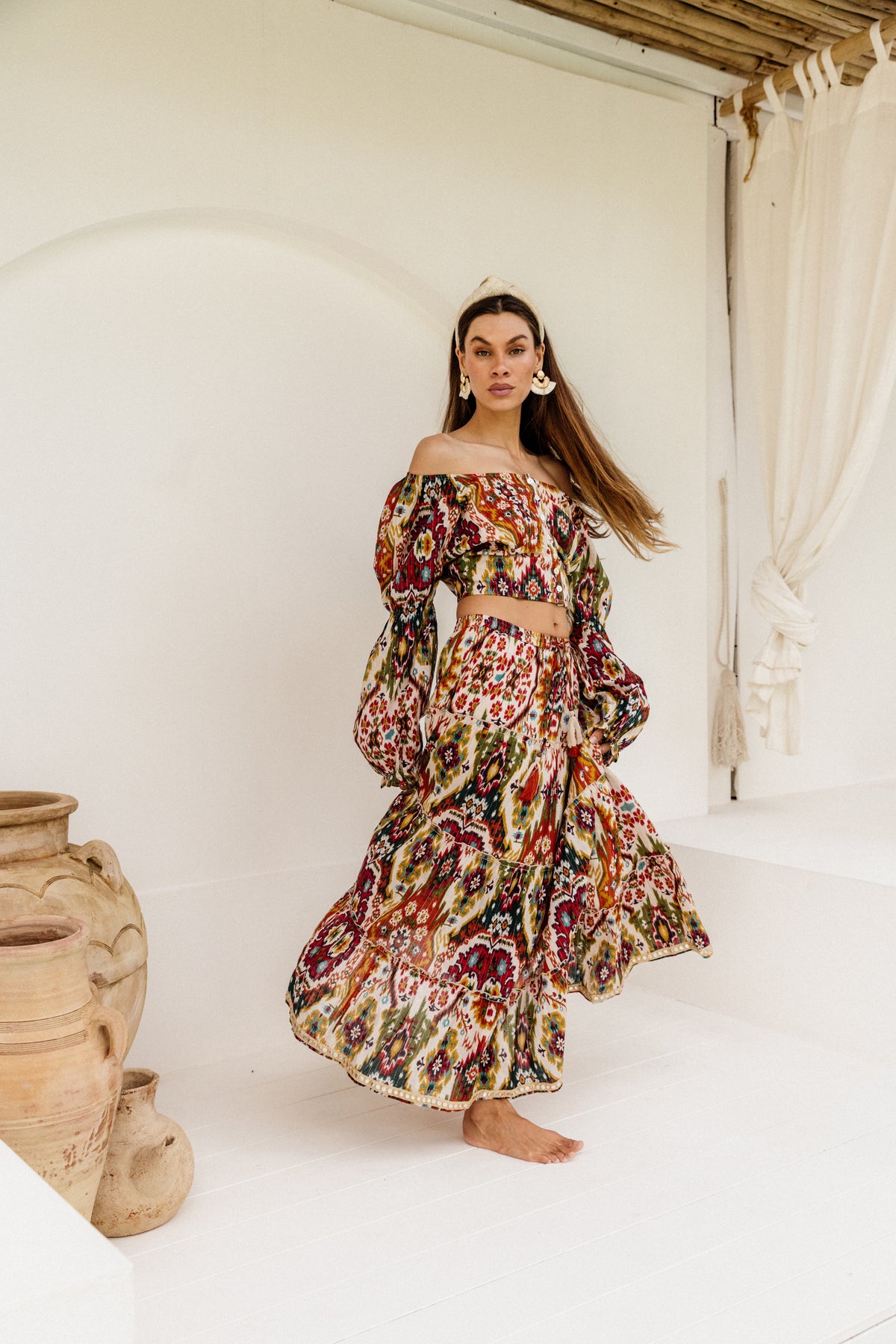 Woman wearing a colorful patterned skirt standing in a bright room with white walls and a wooden ceiling.