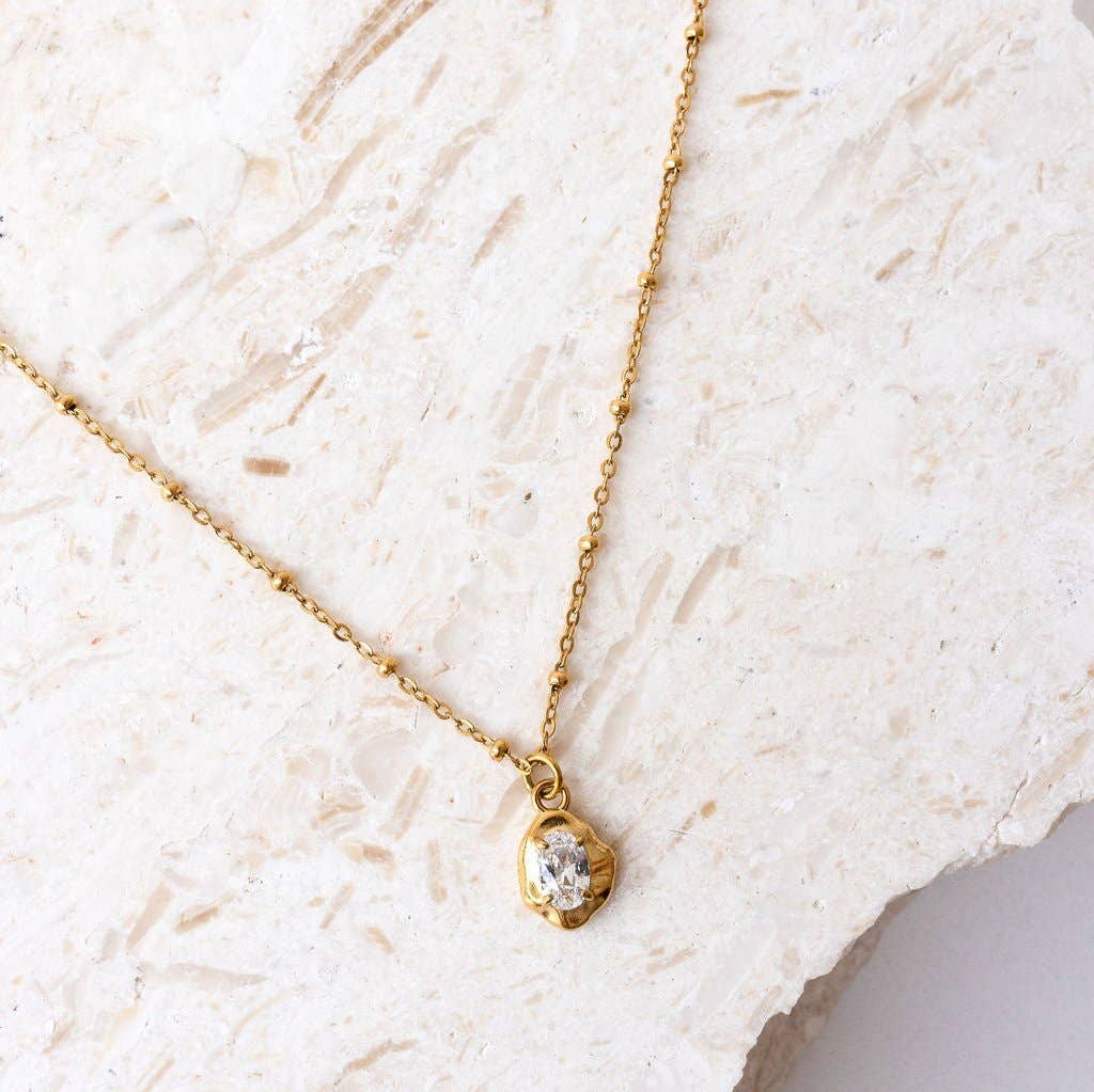 Gold necklace with a zirconia pendant on a textured white surface