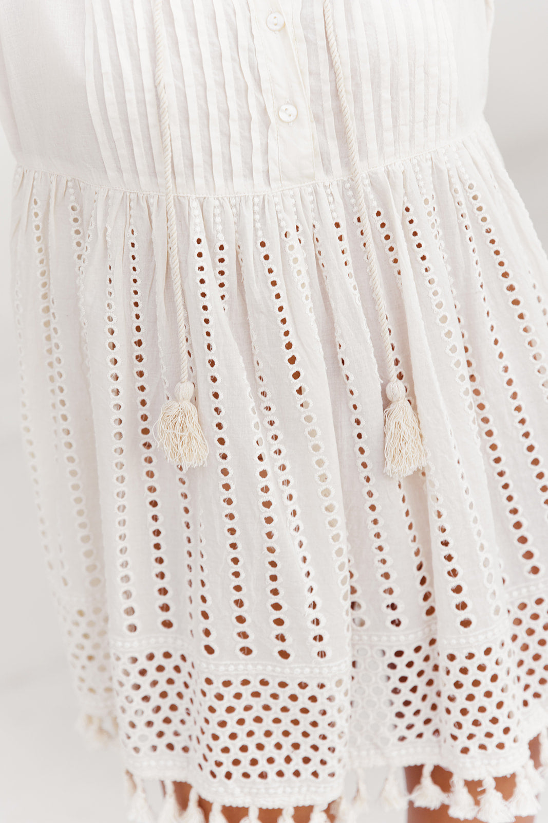 Close-up of a white dress with intricate cut-out pattern on a plain background