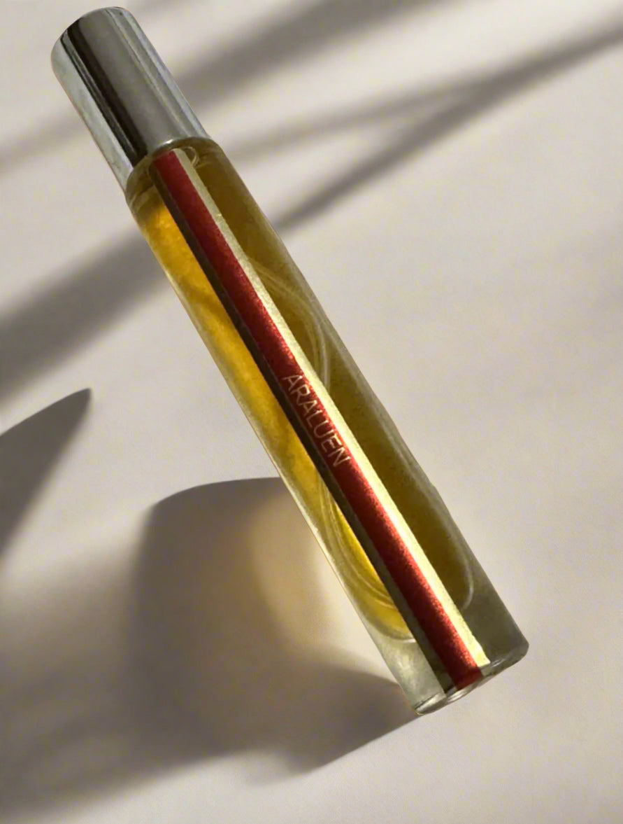 Glass bottle with red and gold design on a textured surface with leaves in the background