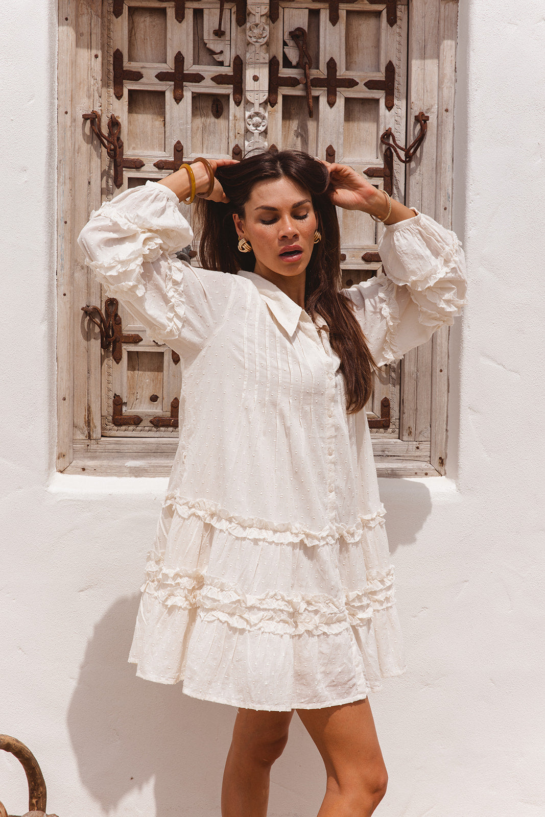 Woman wearing a white dress with long sleeves in front of a rustic wooden door.