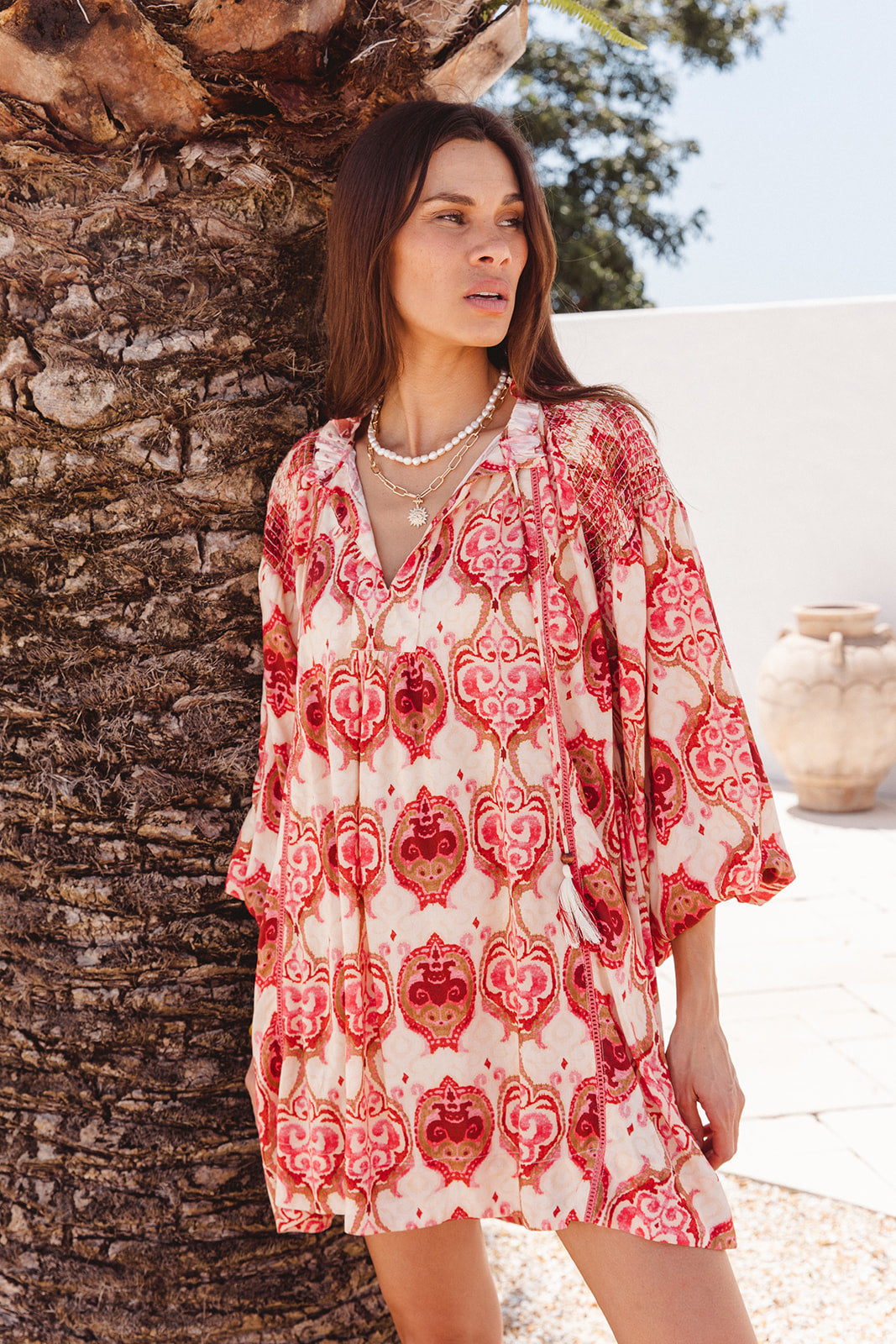Woman wearing a red and white patterned dress standing next to a palm tree.