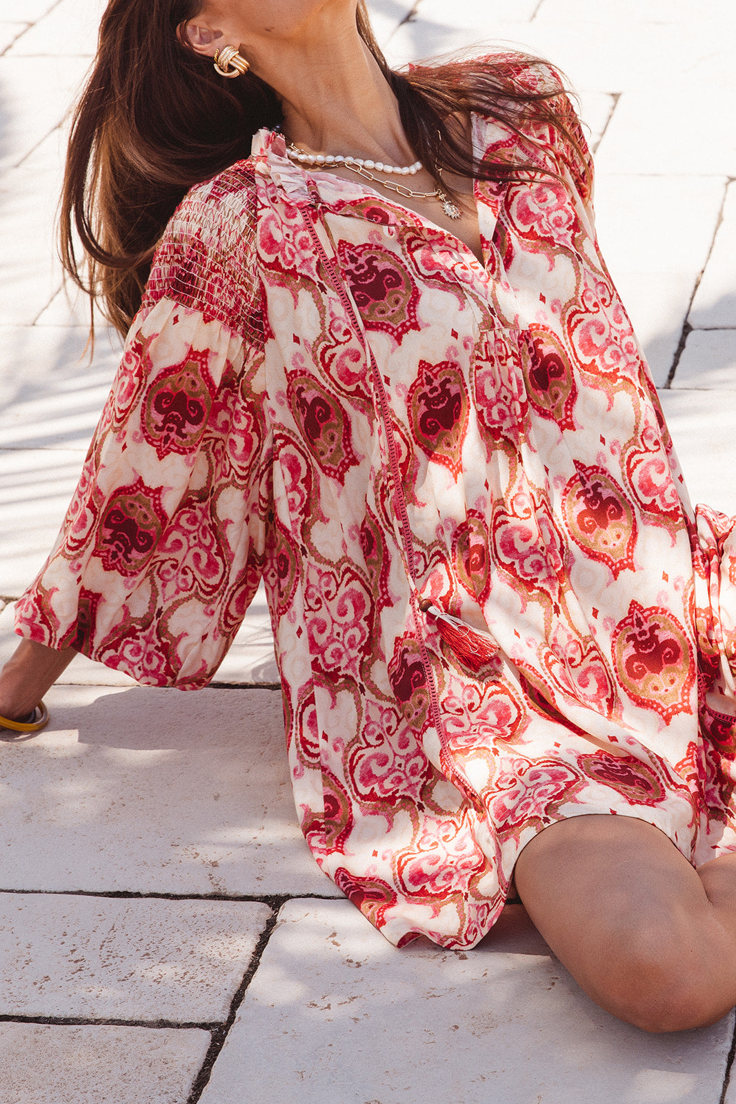 Person wearing a red and white patterned dress sitting on a paved floor.