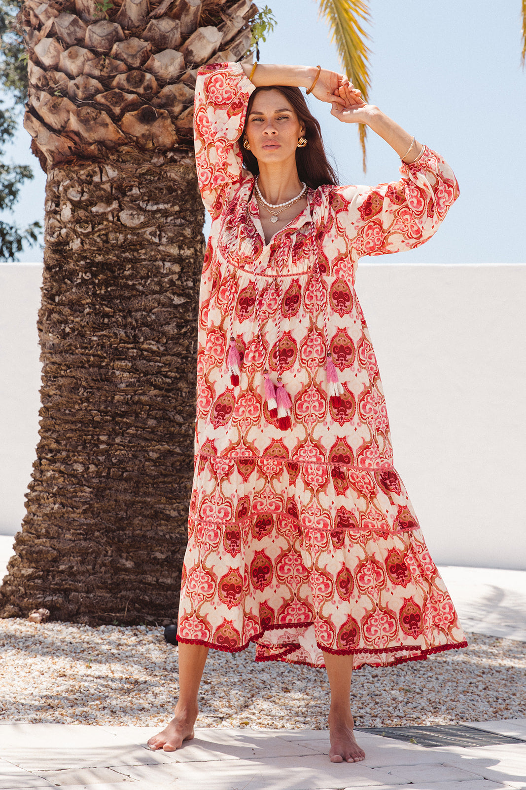 Woman in a red and white patterned dress standing next to a palm tree