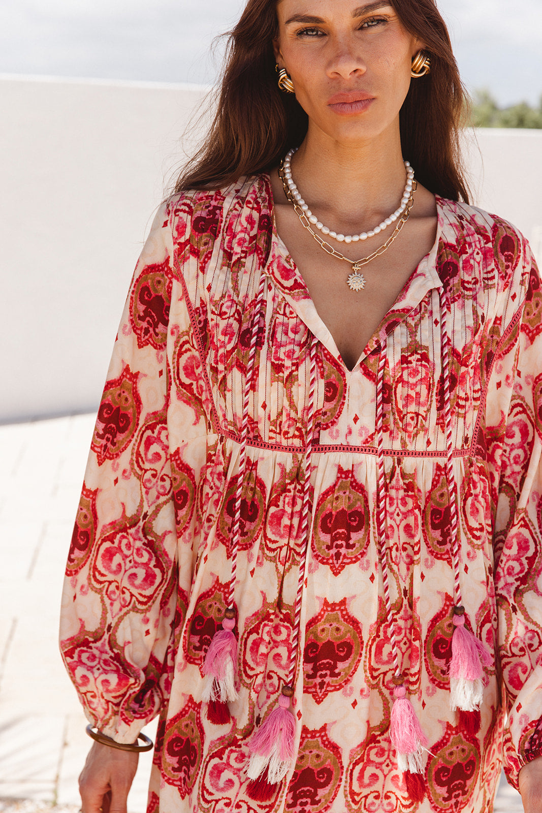 Woman wearing a red and white patterned dress with tassels outdoors.