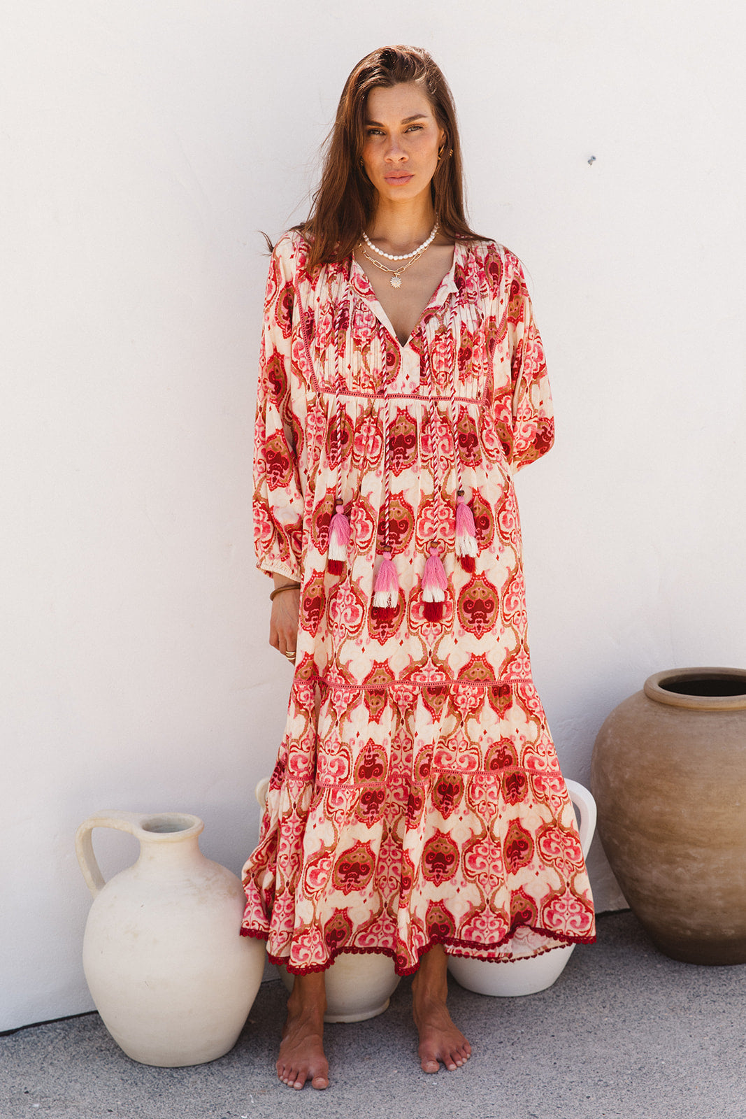 Woman wearing a red and white patterned dress standing against a white wall with decorative vases.