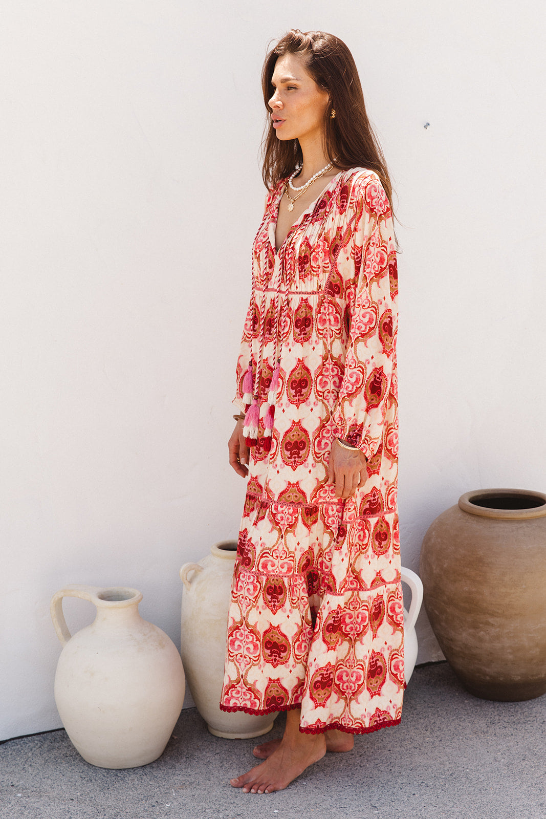 Woman wearing a red and white patterned dress standing against a white wall with decorative vases.