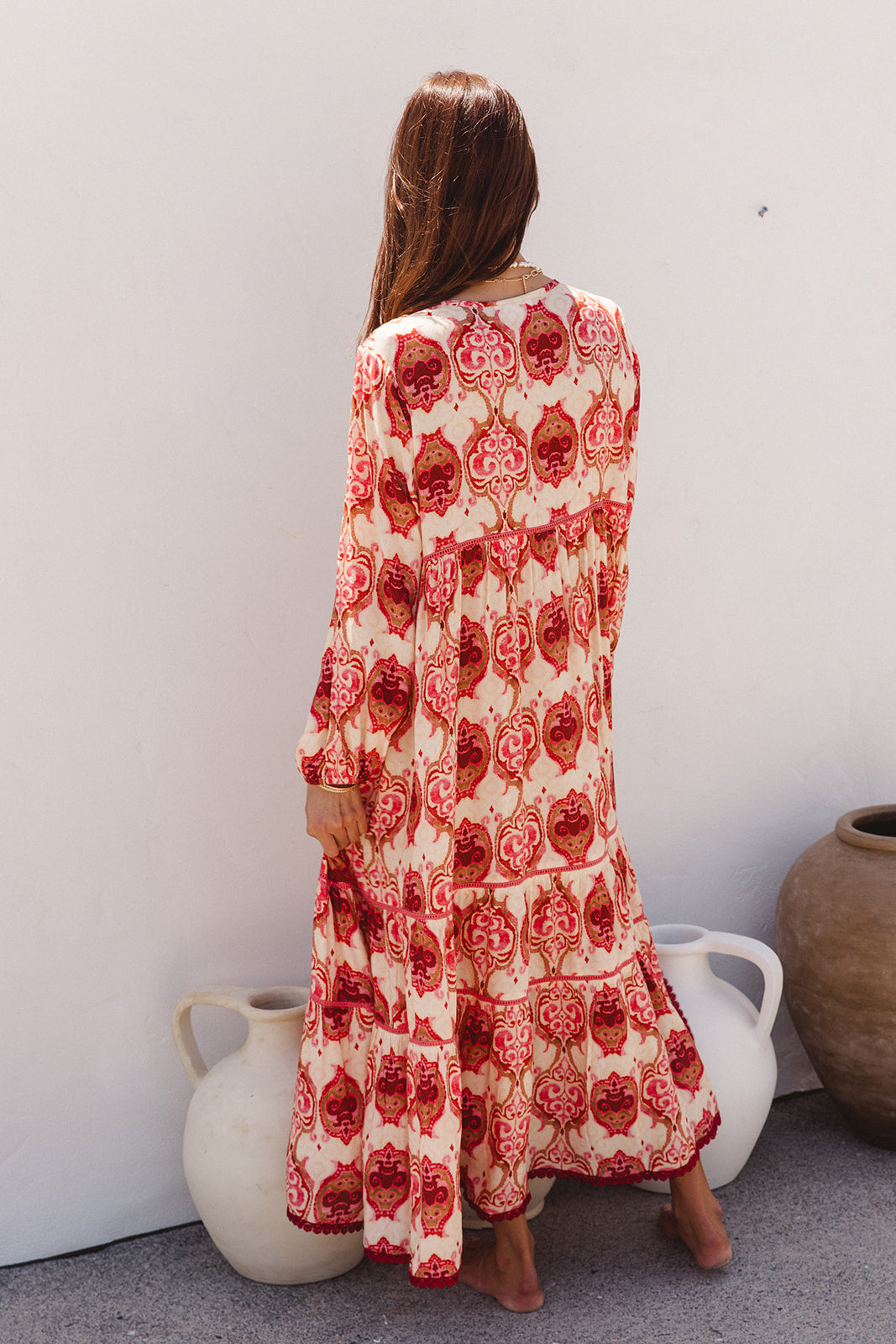 Woman wearing a red and white patterned dress standing against a white wall with two ceramic pots.