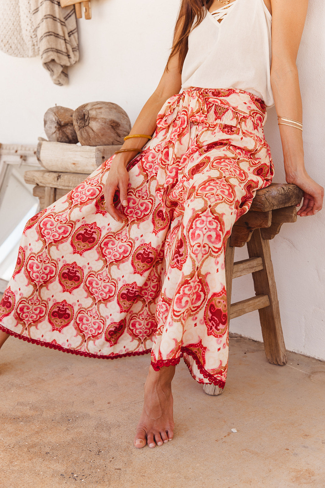 Person wearing a red and white patterned wide pants sitting on a wooden stool.