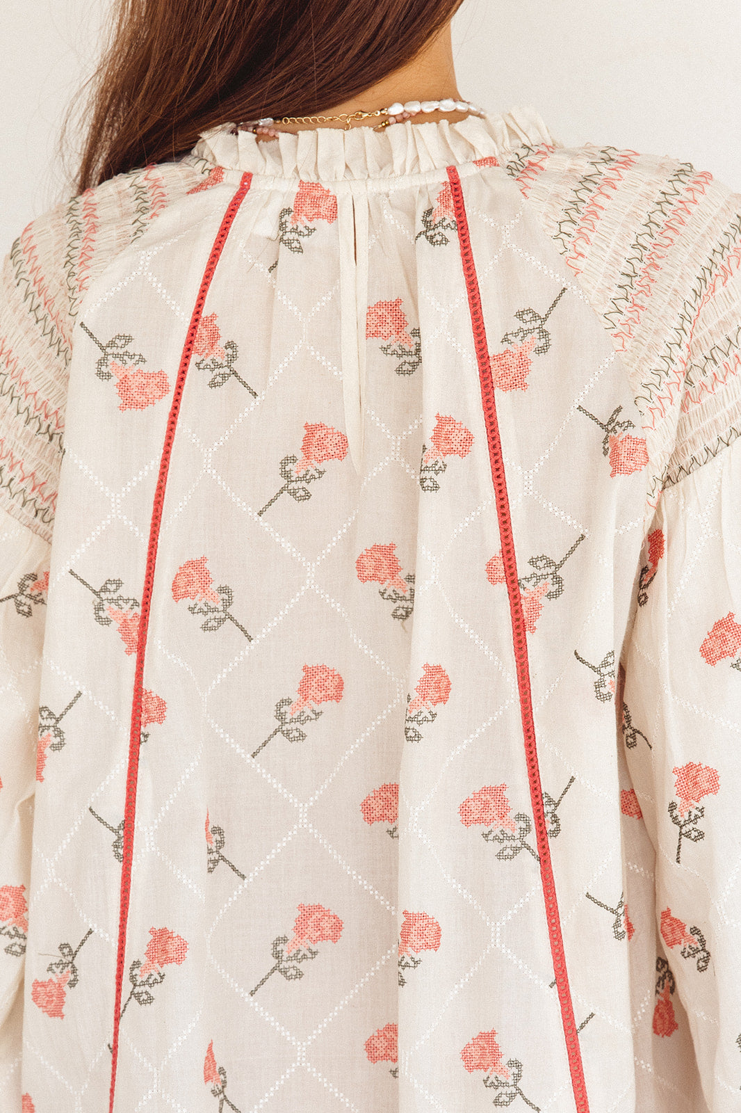Close-up of a white garment with floral embroidery and red stitching.