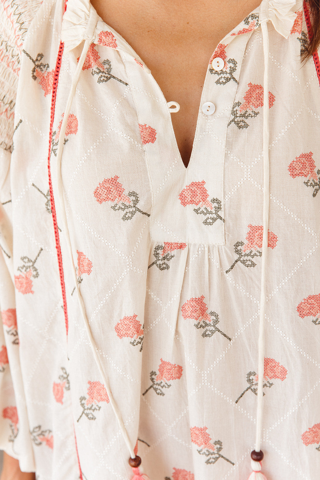 Close-up of a white blouse with floral patterns and drawstrings.