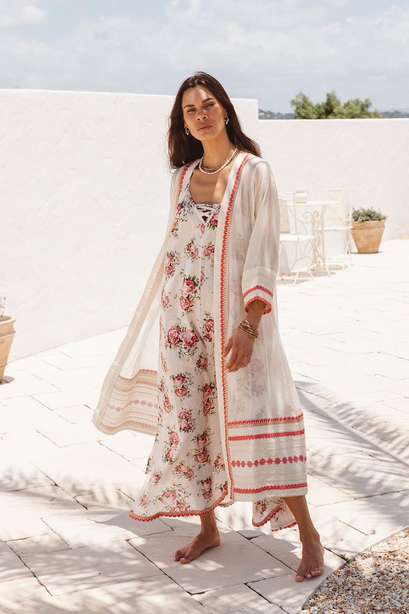 Woman in a floral dress and cover-up standing on a sunlit terrace.
