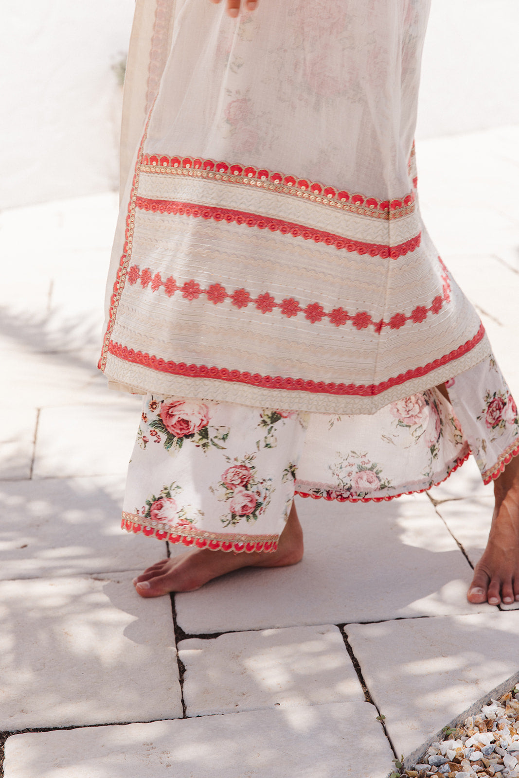 Close-up of a white dress and cover up with floral pattern and red embroidery on a stone pavement.