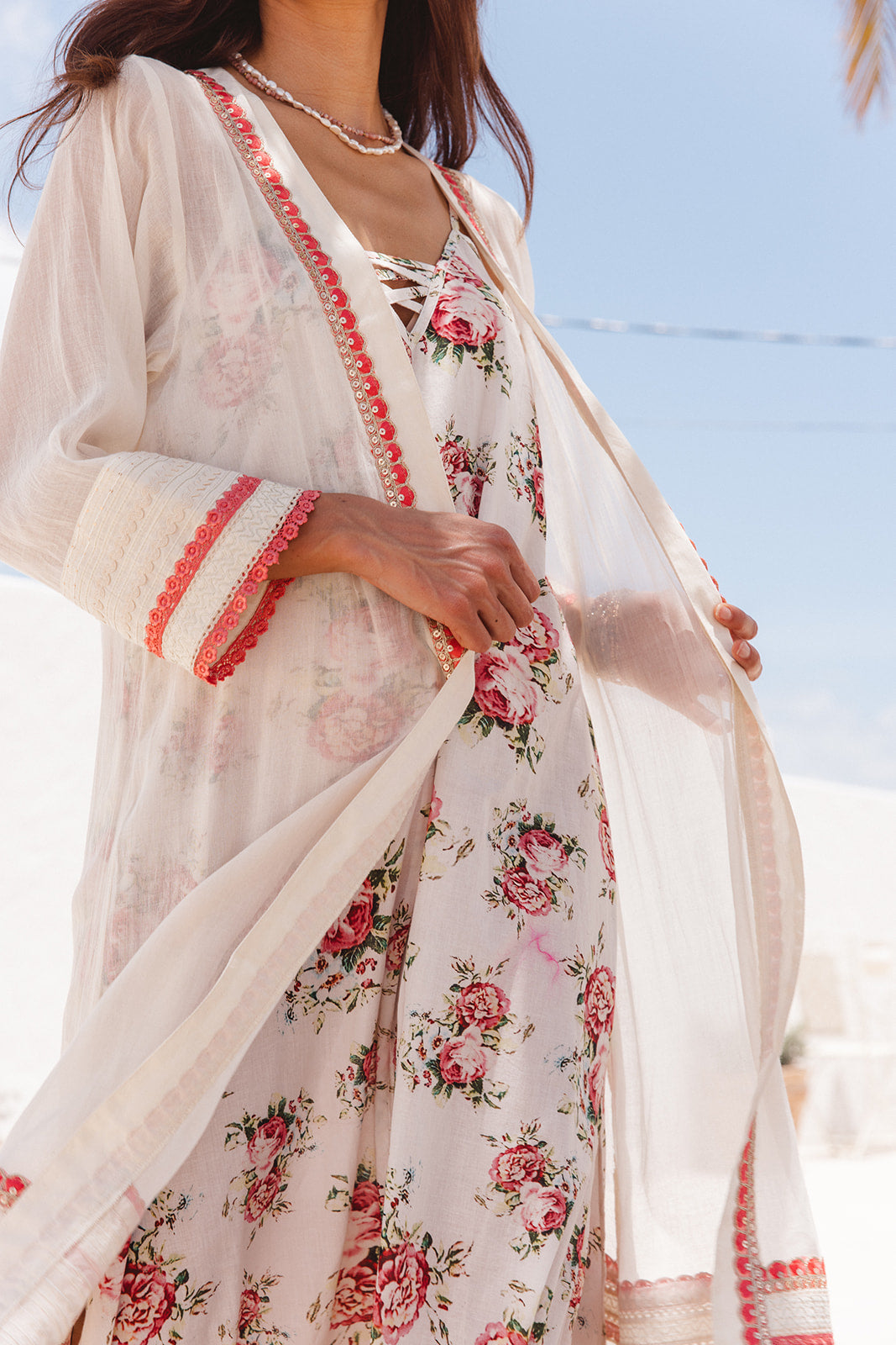 Woman wearing a floral dress with a sheer white overlayer against a clear blue sky.