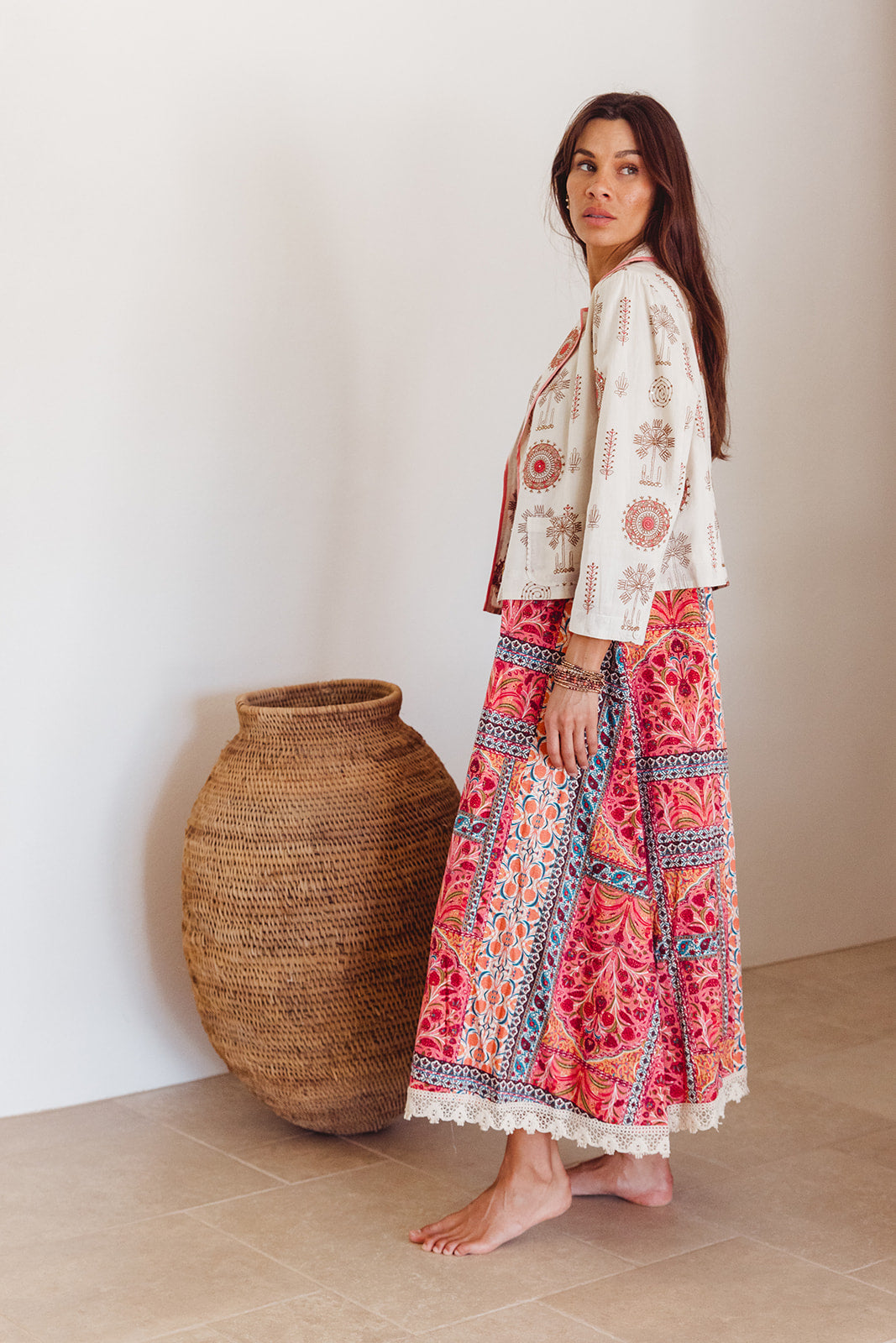 Woman wearing a floral outfit standing next to a woven basket indoors.