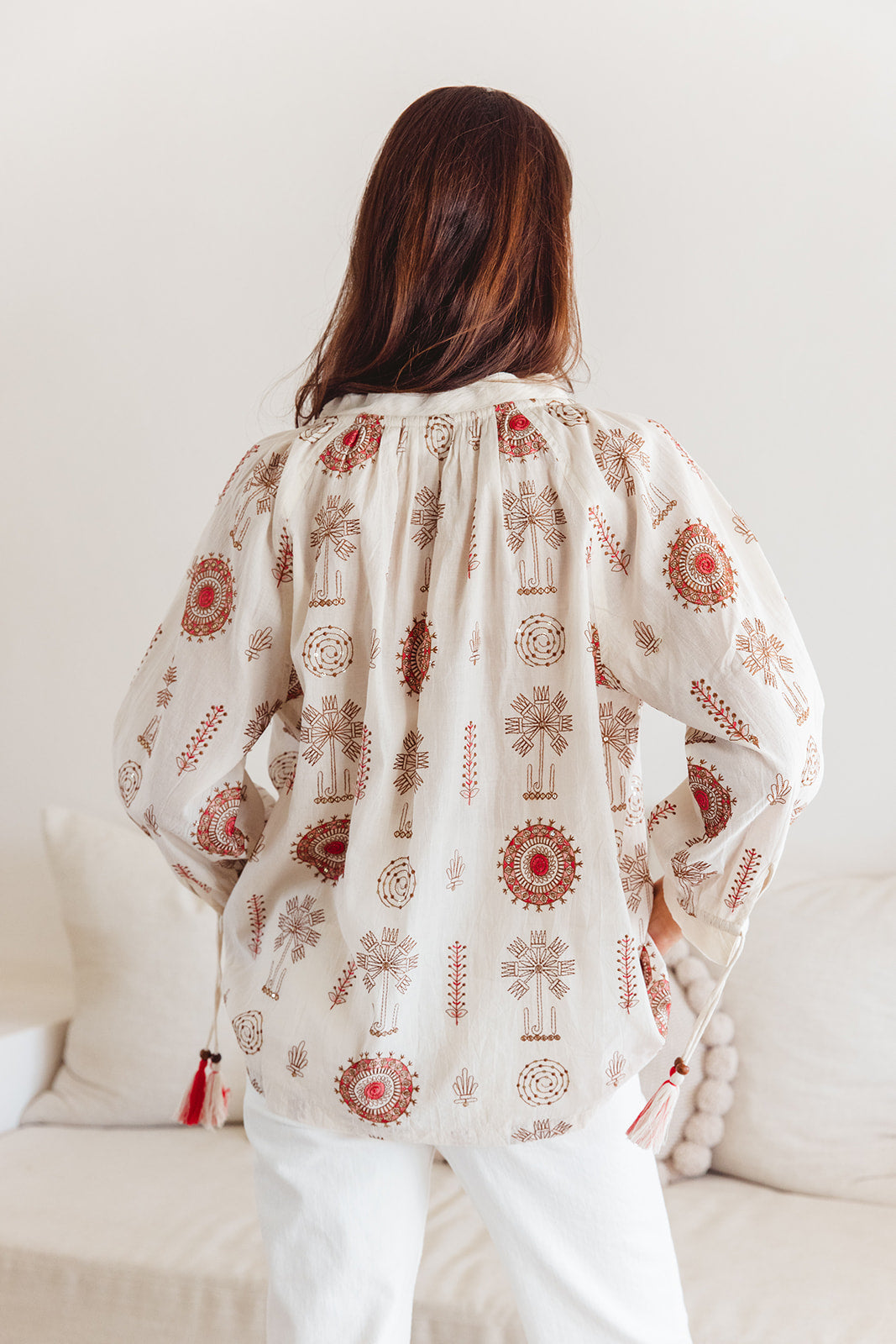 Person wearing a patterned blouse standing by a white couch.