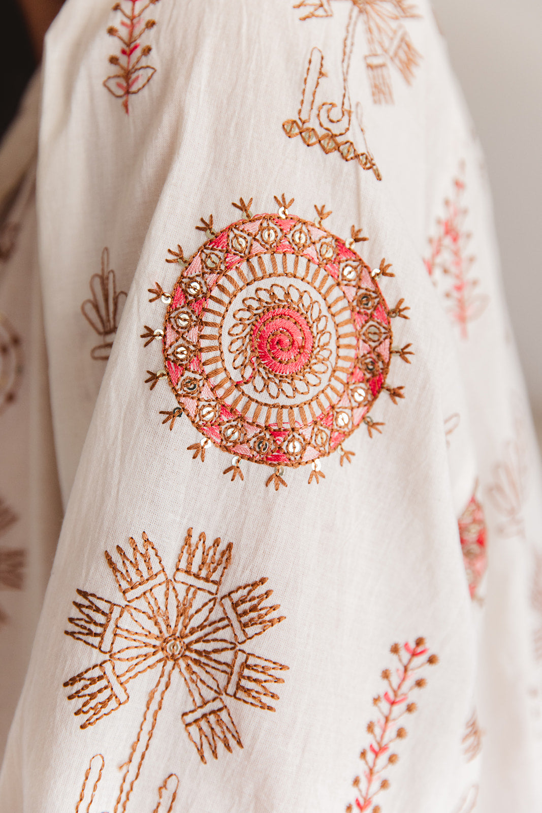 Close-up of a white fabric with intricate gold and pink embroidery