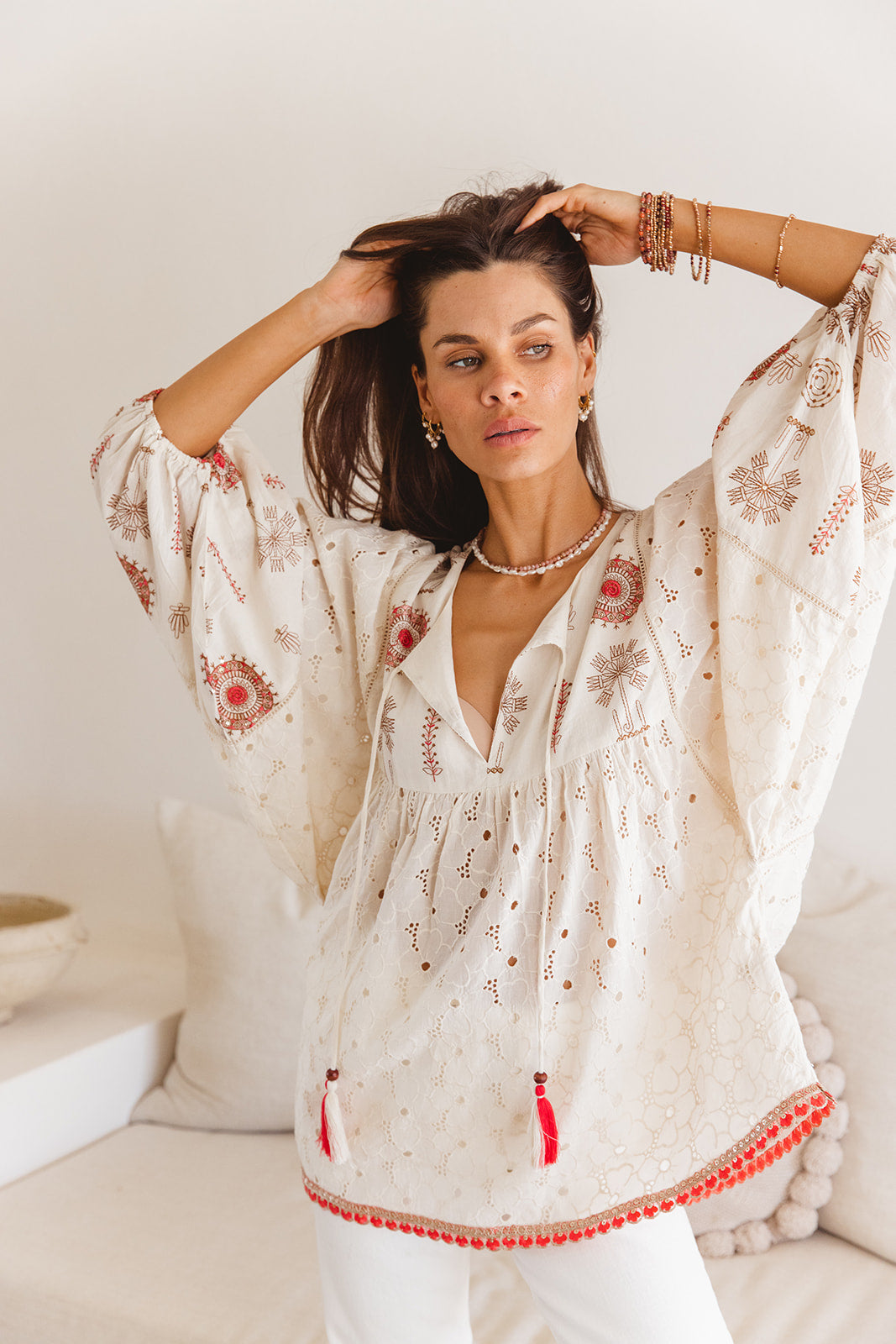 Woman wearing a white embroidered blouse with red details in a minimal indoor setting