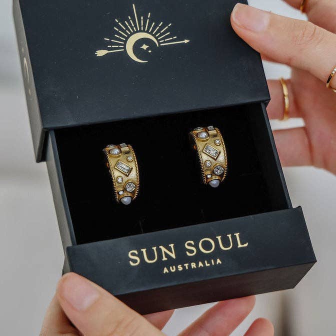 Gold earrings in a 'Sun Soul Australia' box held by a hand.