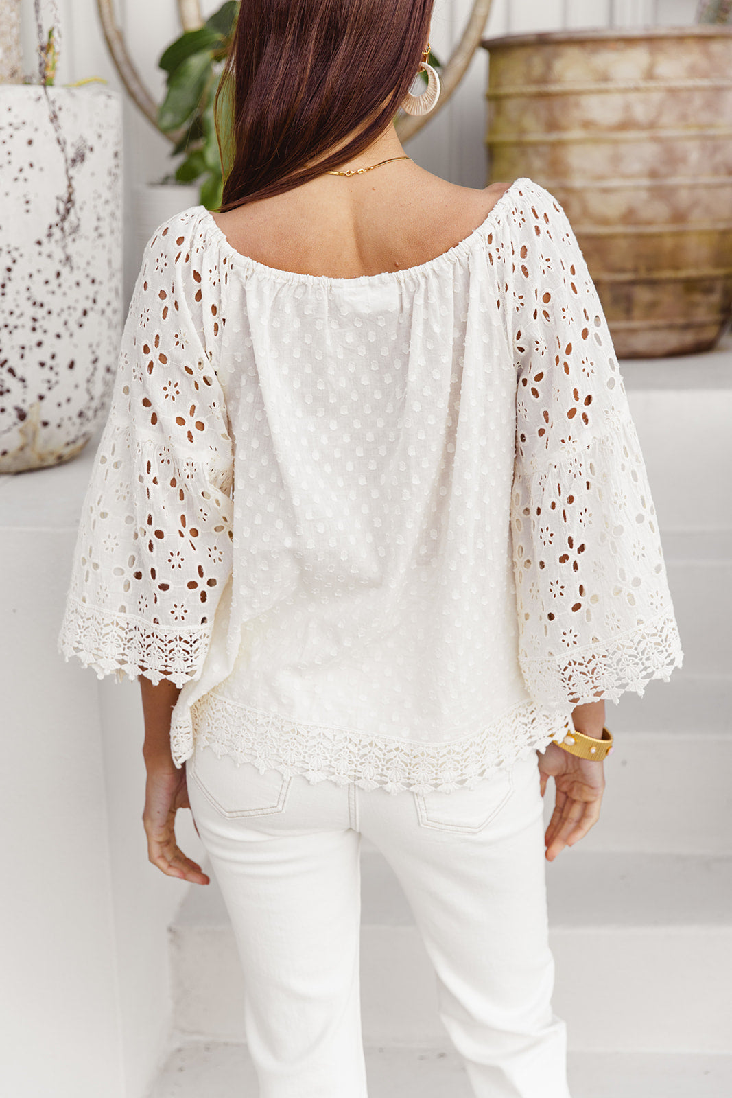 Woman wearing a white lace blouse and white pants in an indoor setting.