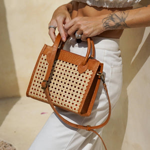 Person holding a brown handbag with a patterned design against a neutral background