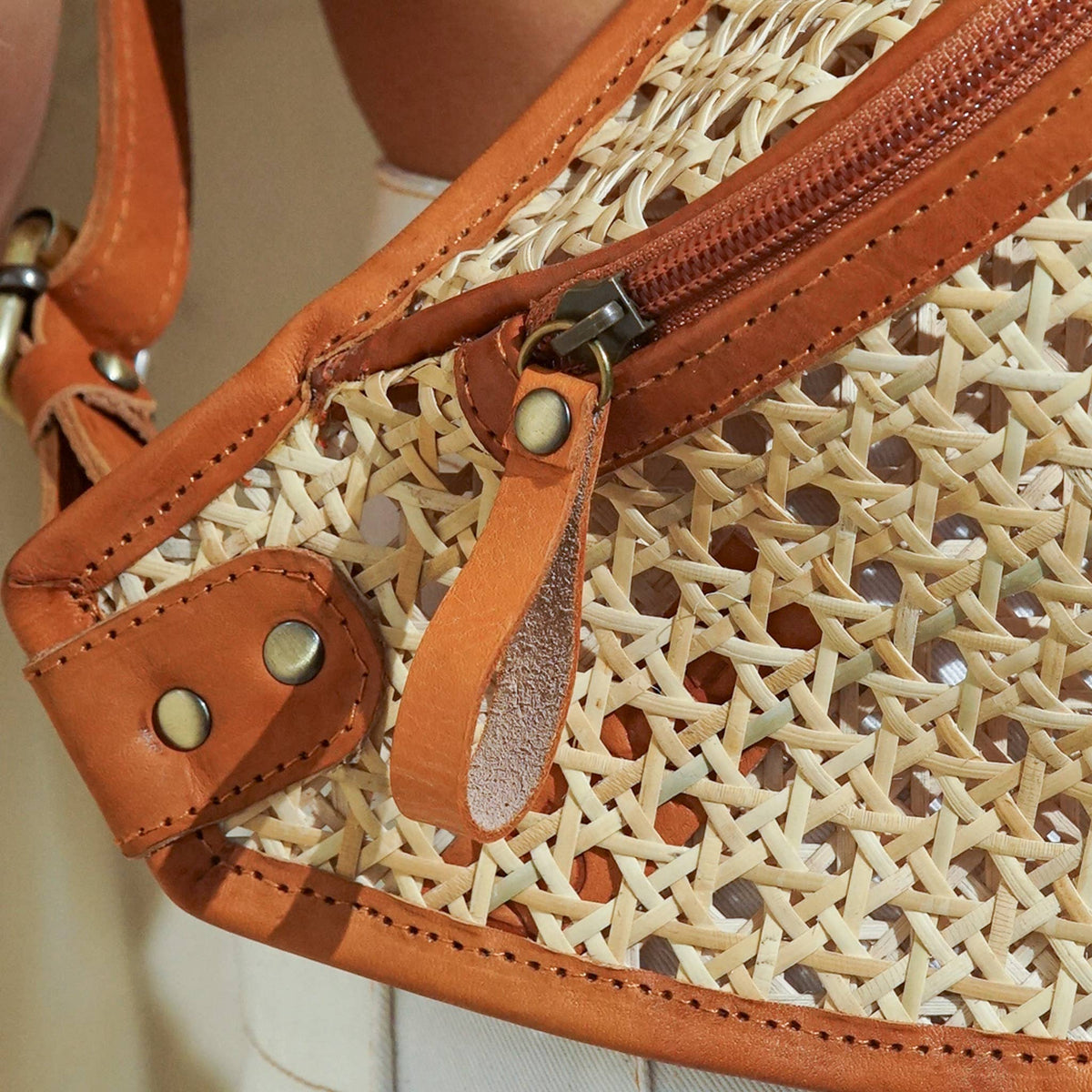 Close-up of a woven handbag with leather accents and a zipper.