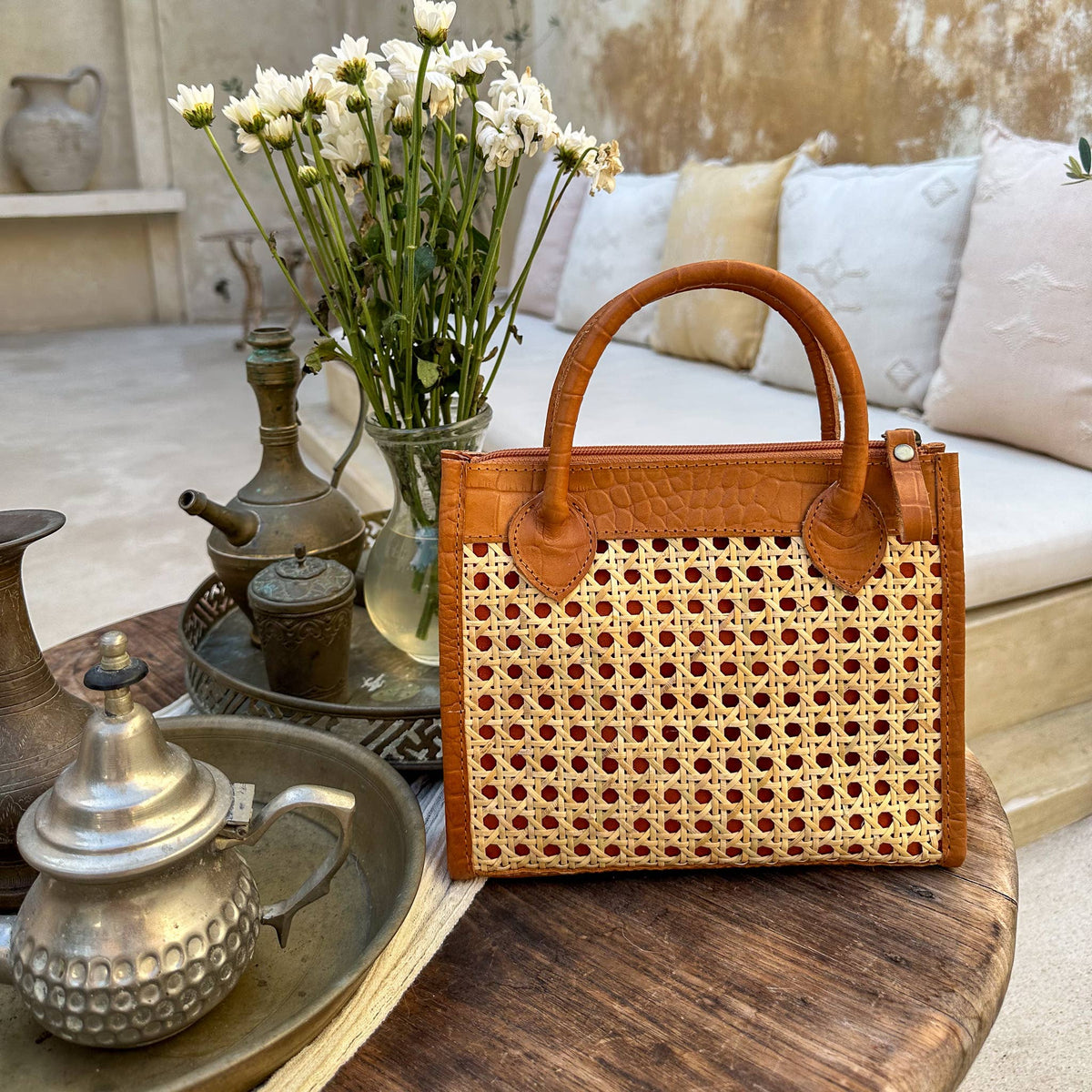 Woven handbag on a wooden table with decorative items and a couch in the background